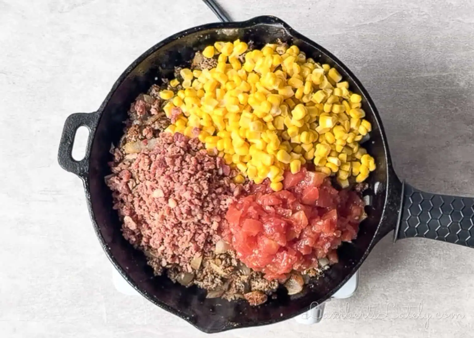 corn, tomatoes, and bacon added to a cast iron skillet.