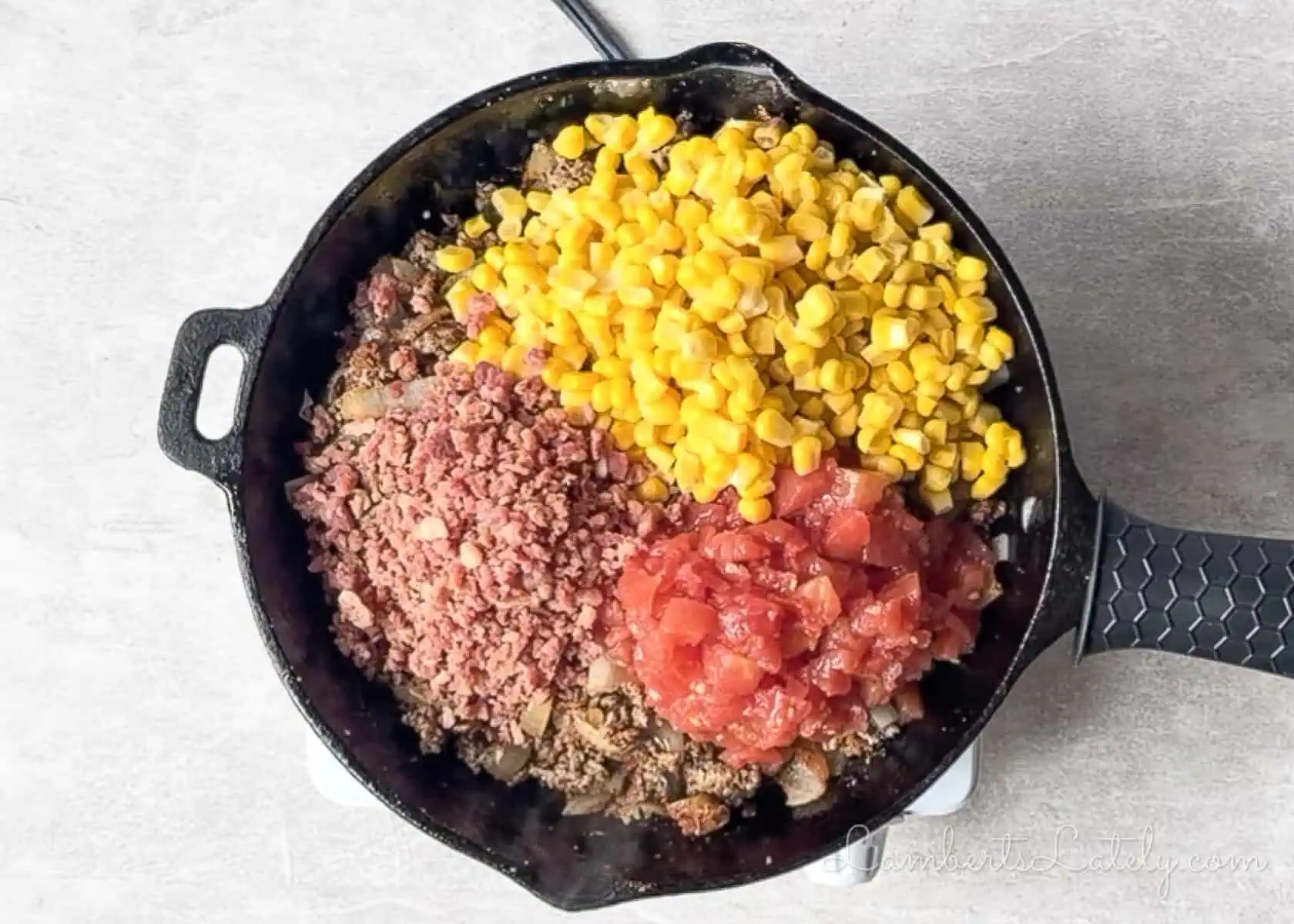 corn, tomatoes, and bacon added to a cast iron skillet.