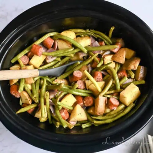 crock pot full of swamp potatoes with green beans, sausage, and red onion.