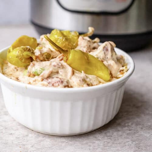 bowl of mississippi chicken, topped with pepperoncini peppers, in front of an instant pot.