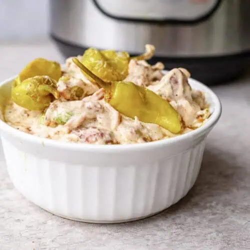 bowl of mississippi chicken, topped with pepperoncini peppers, in front of an instant pot.