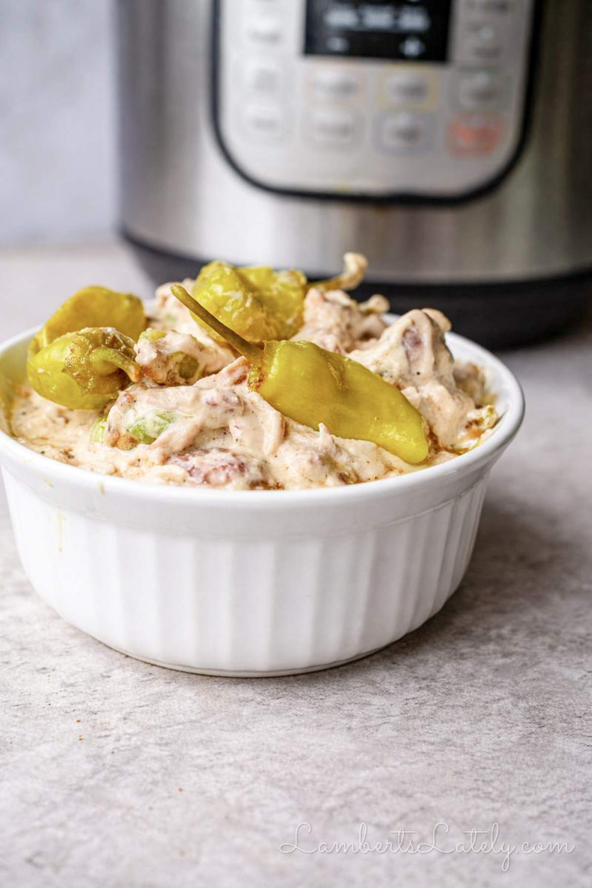 bowl of mississippi chicken, topped with pepperoncini peppers, in front of an instant pot.