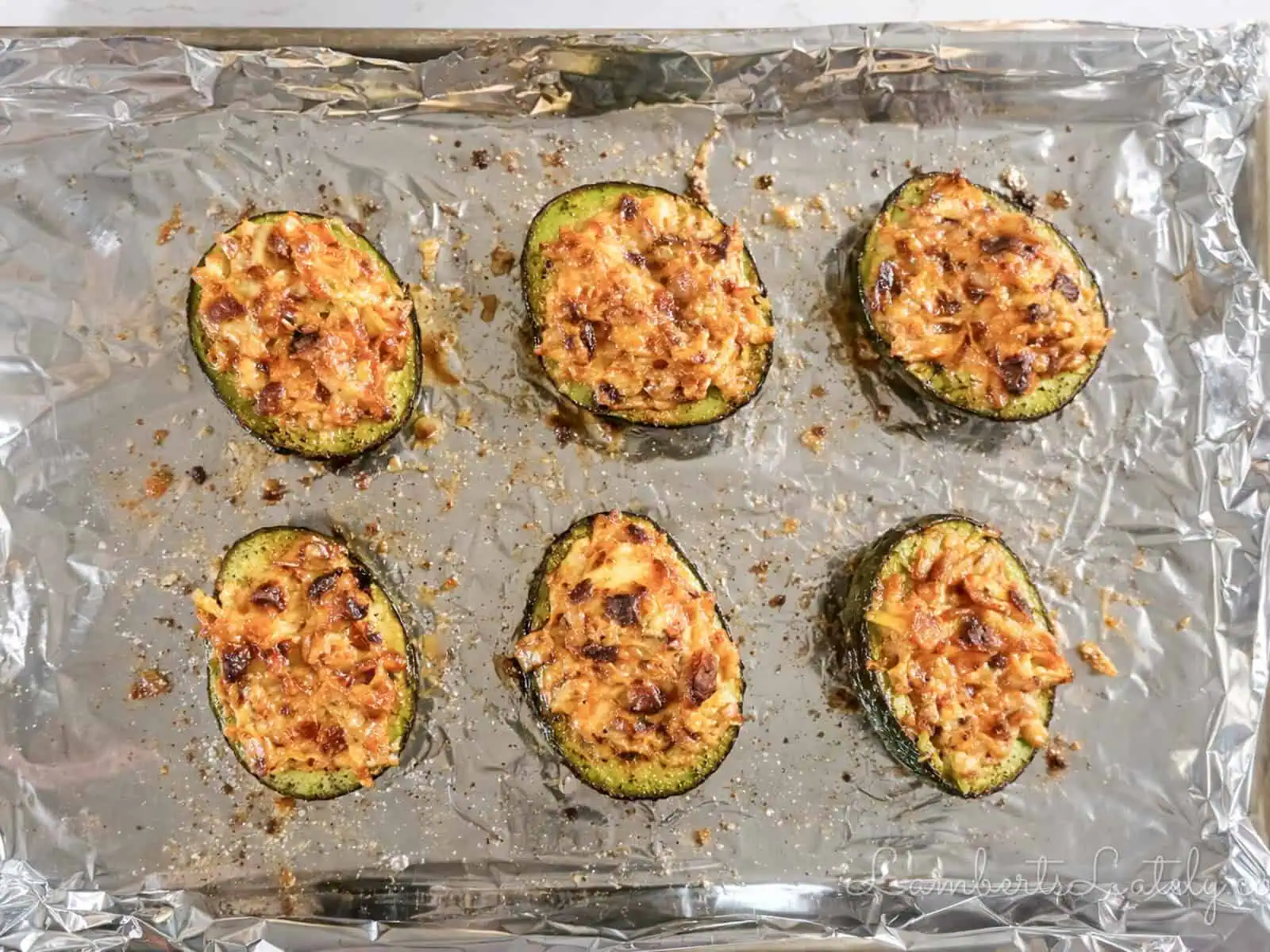 baked avocado halves on a lined baking sheet.