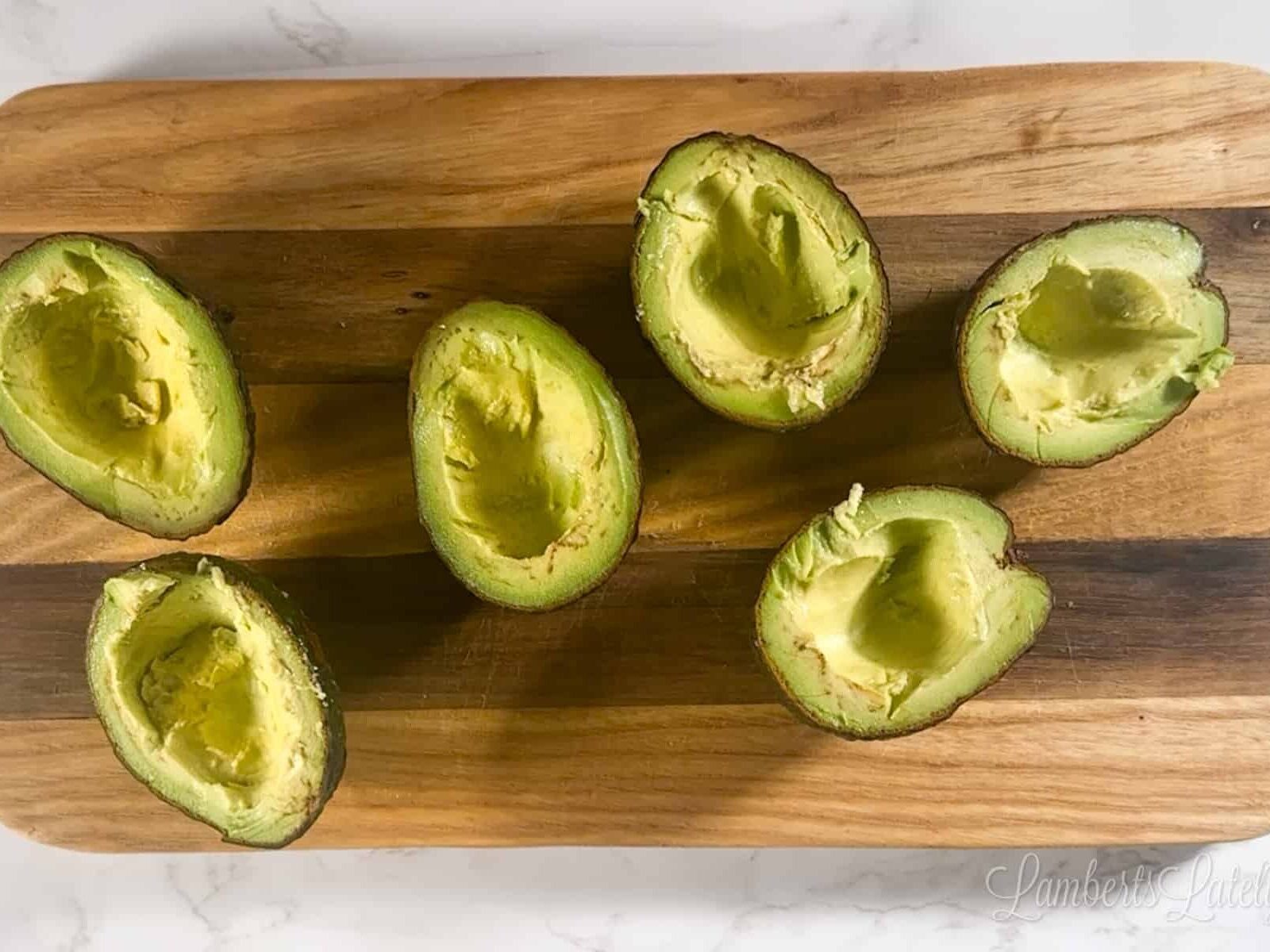 avocados with some of the flesh scooped out on a cutting board.