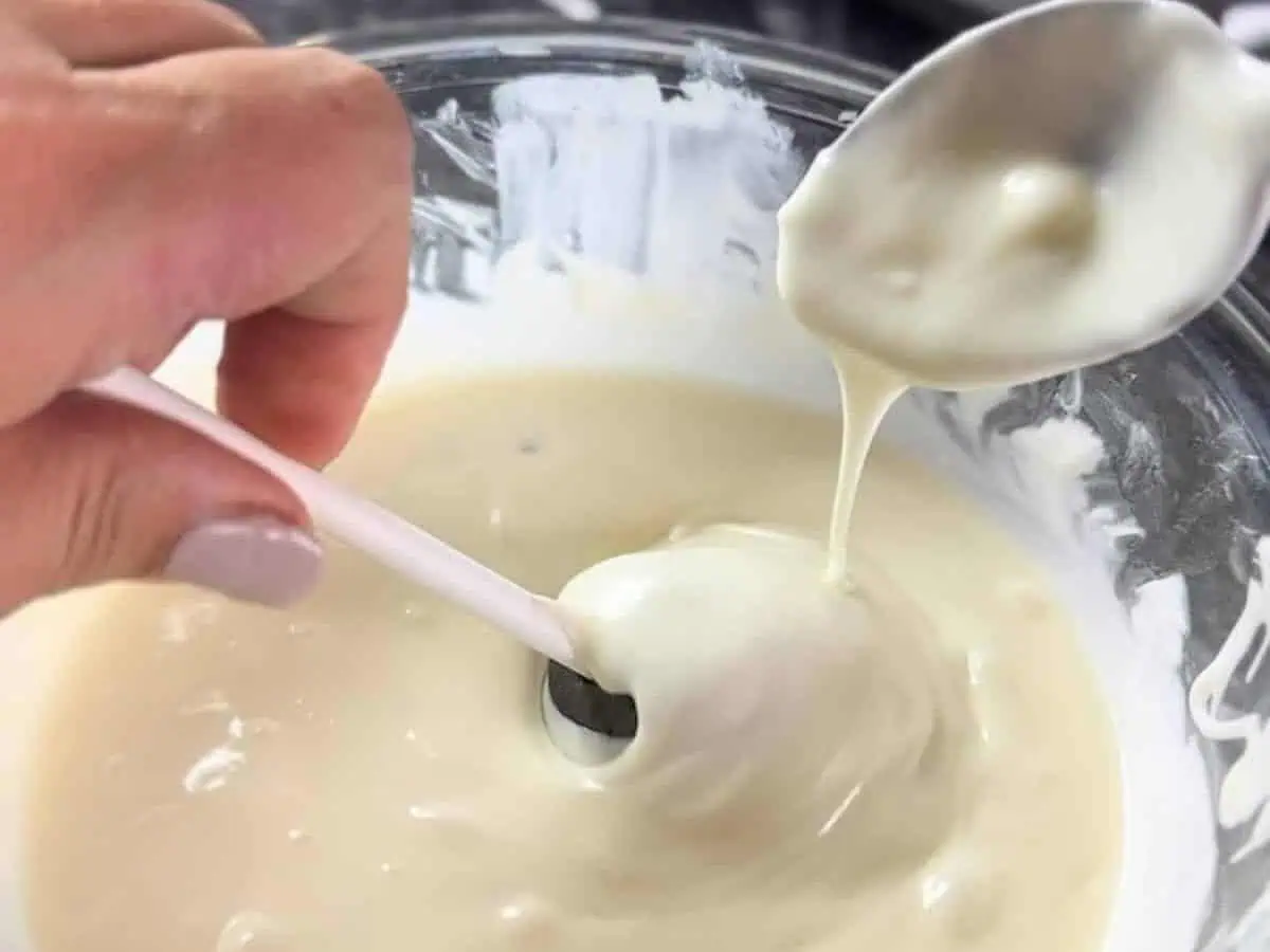 covering oreo cake pop in melted white chocolate using a spoon.