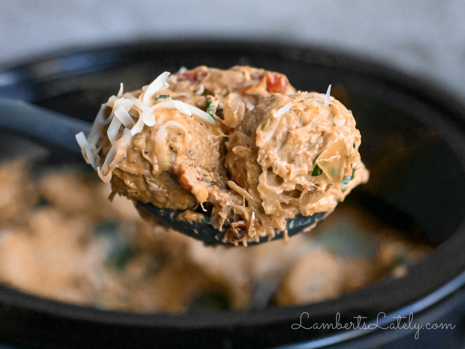 two chicken meatballs on a spoon, covered in a creamy tomato sauce and cheese, in front of a crock pot.