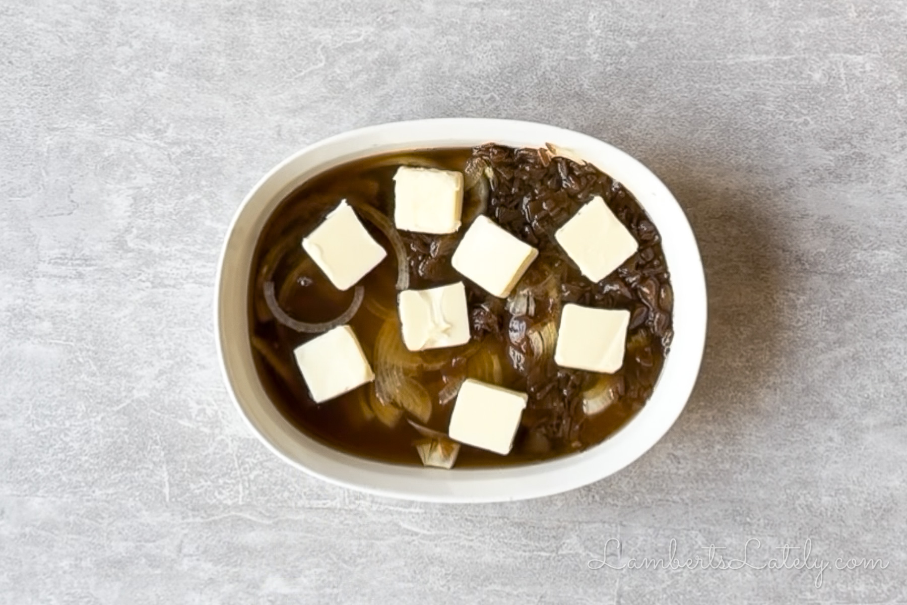 butter, french onion soup, onions, rice, and broth combined in a casserole dish.