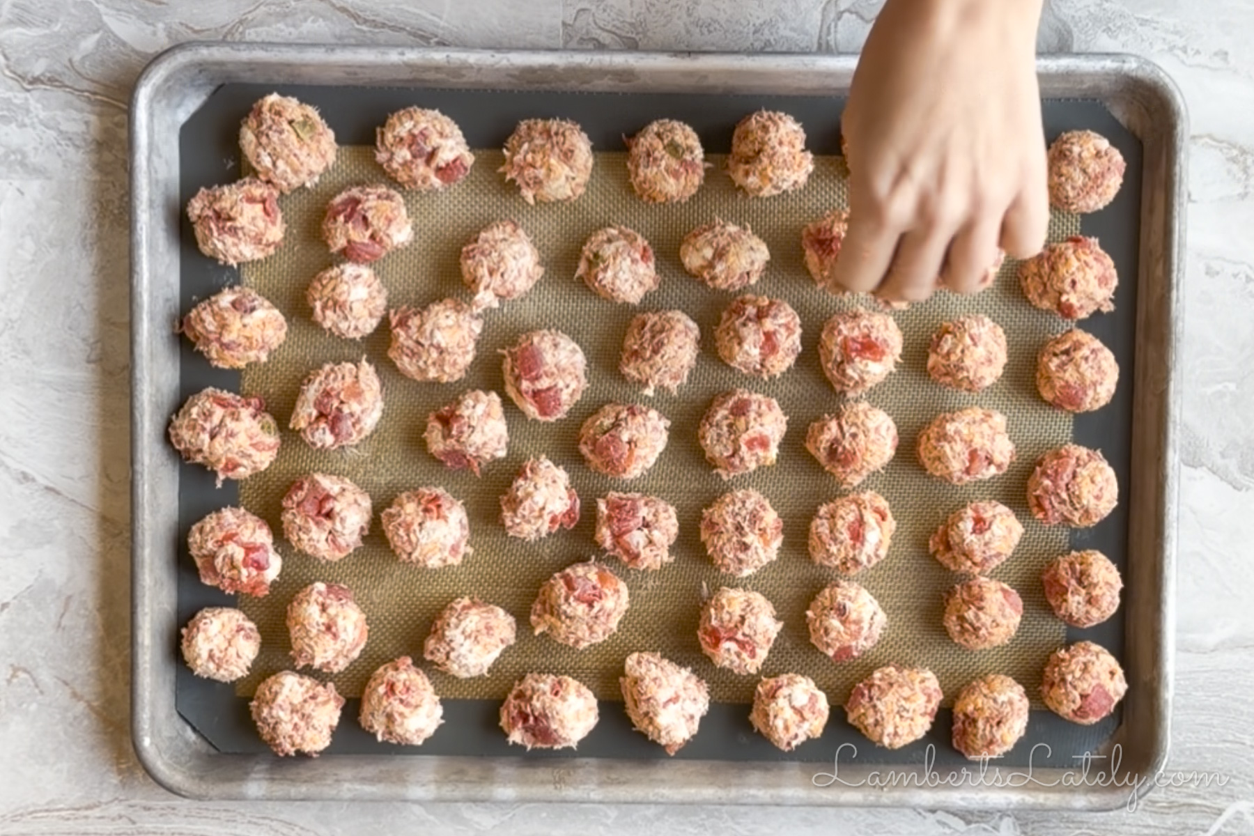 placing rolled rotel sausage balls on a lined baking sheet.