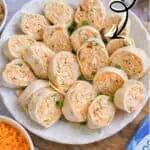 Buffalo chicken pinwheels on a white plate, perfect for parties, with dipping sauce.