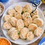Buffalo chicken pinwheels on a white platter with dipping sauces and ingredients.
