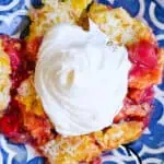 Tropical fruit dump cake with whipped cream on a decorative plate.