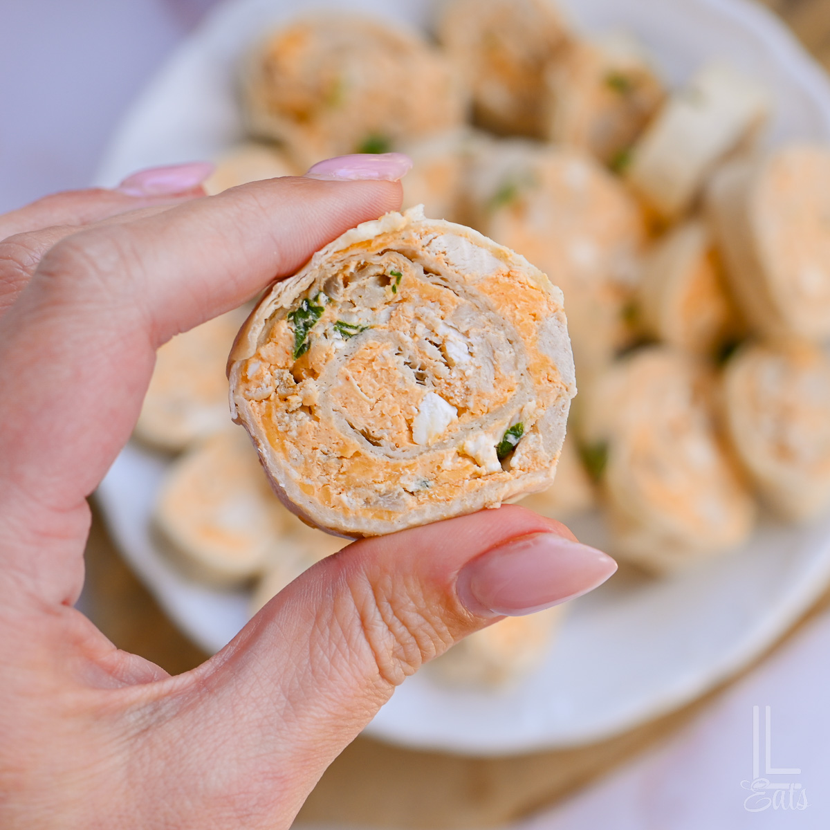 holding a buffalo chicken pinwheel, showing chicken, green onions, and a creamy sauce.