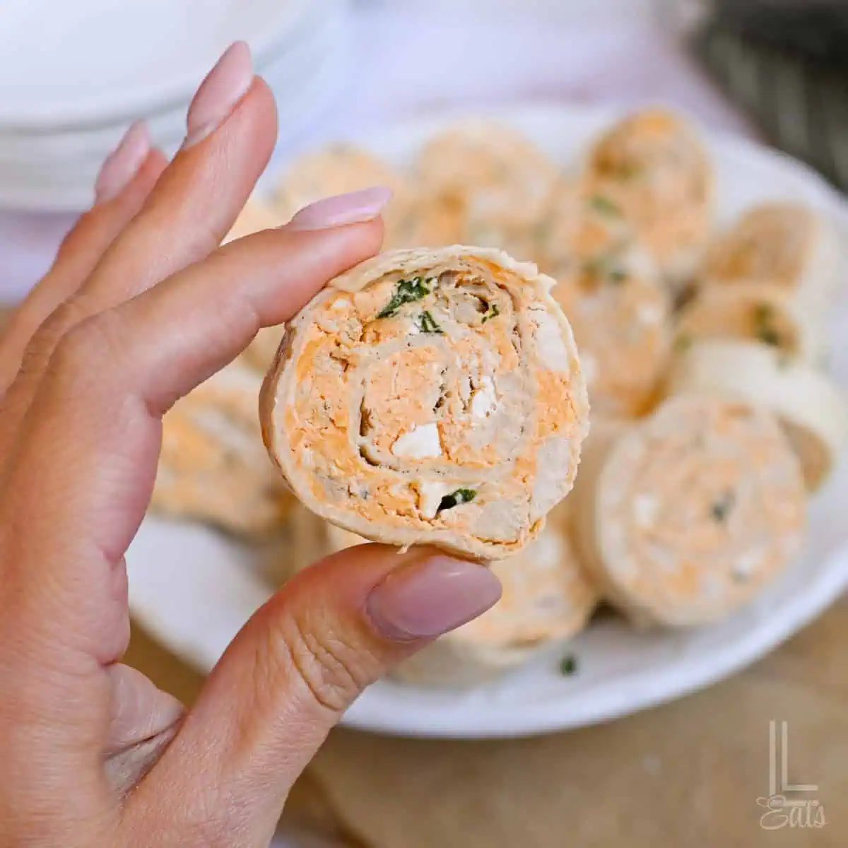 Close-up of a buffalo chicken pinwheel held by hand with more pinwheels in background.