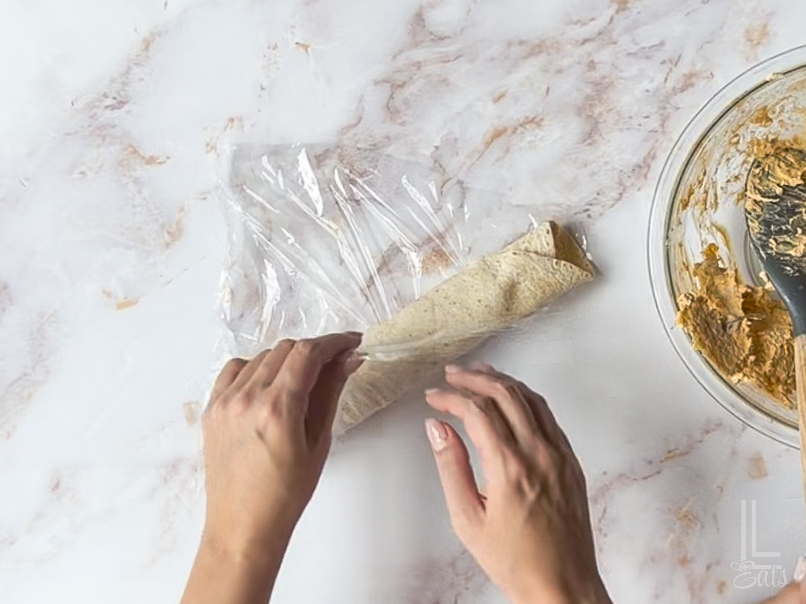 wrapping tortilla roll-up in plastic wrap.