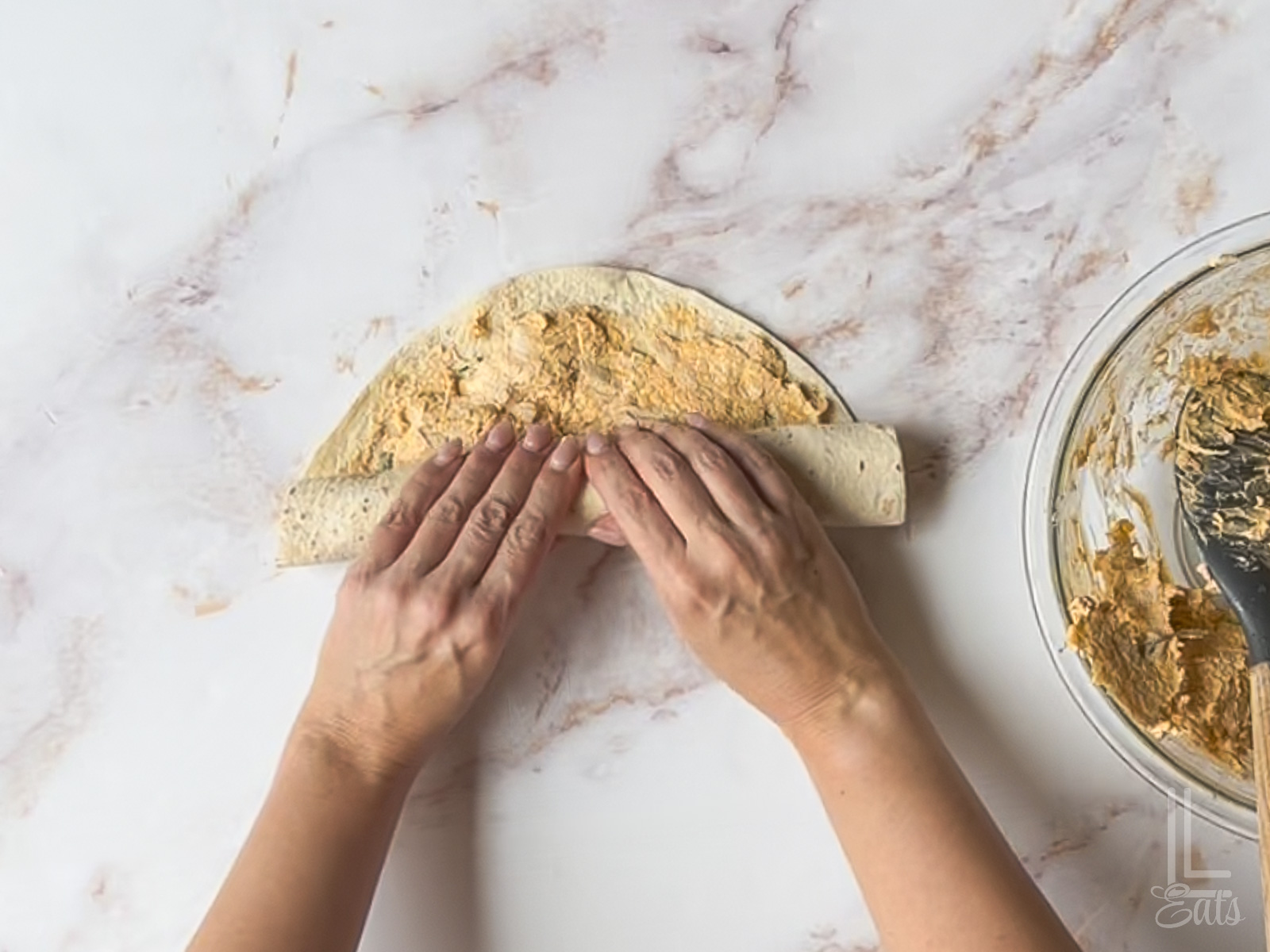 rolling up the tortilla covered in buffalo chicken mixture.
