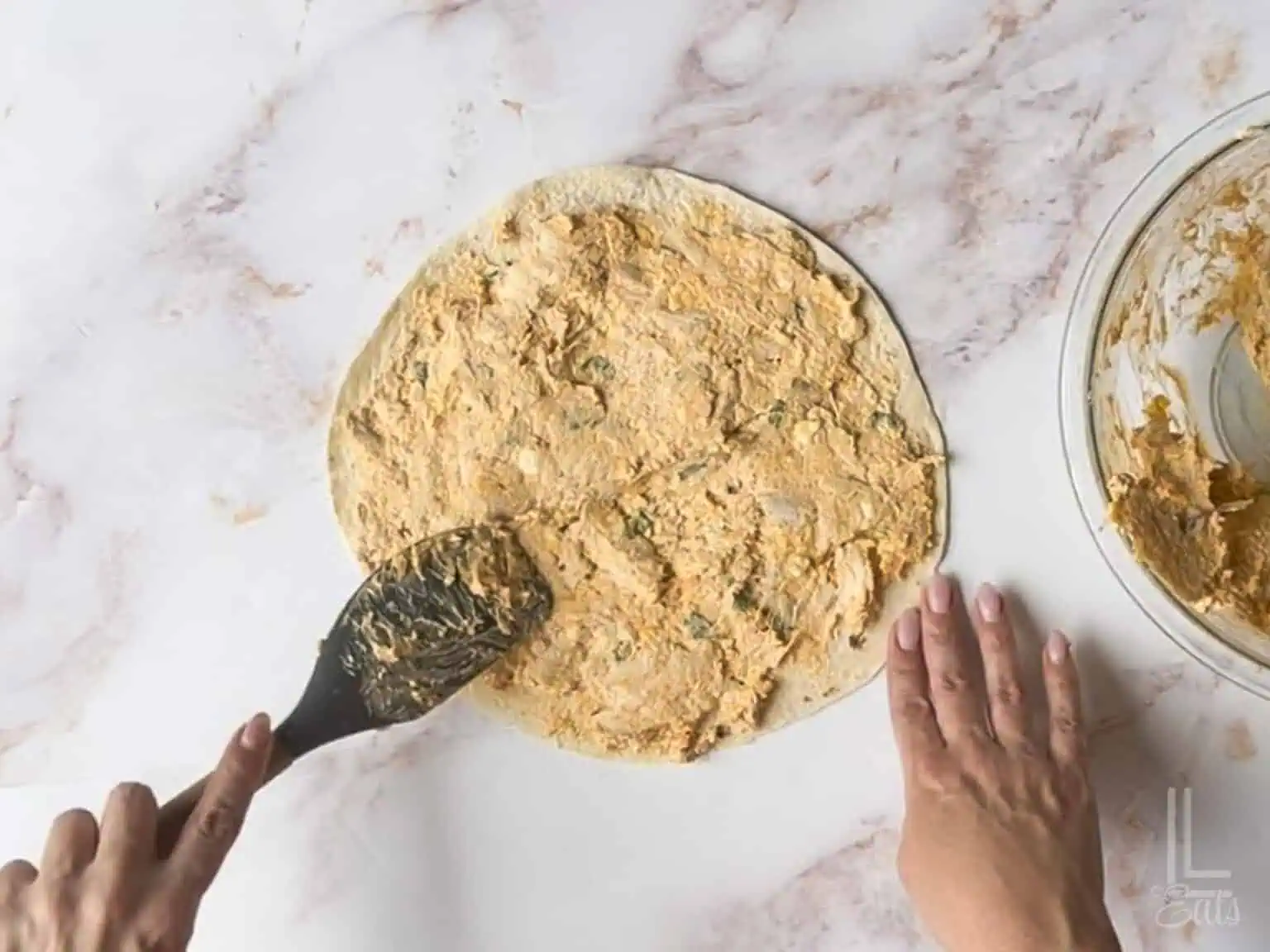 spreading buffalo cream cheese mixture onto a large tortilla.