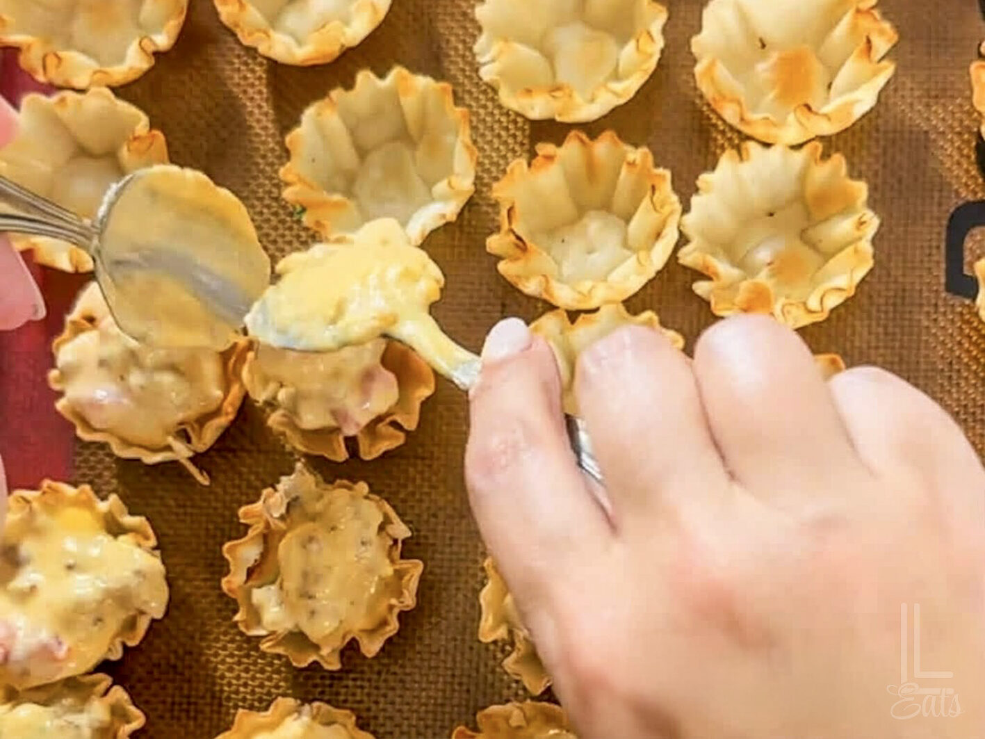 spooning the melted cheese mixture into phyllo cups on a baking sheet.