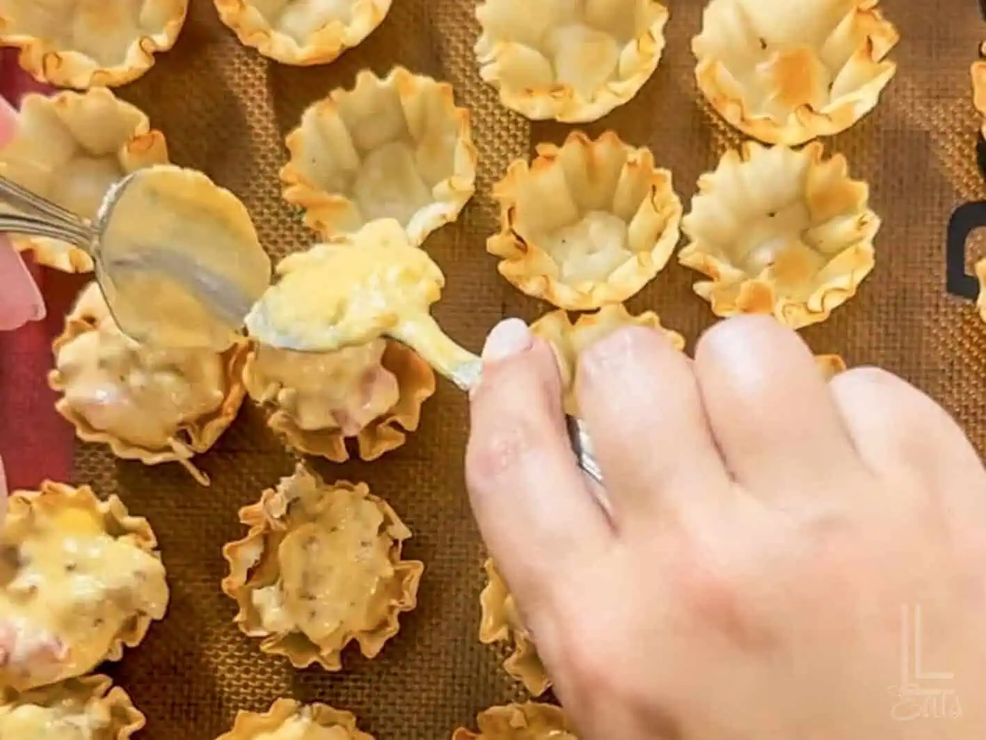 spooning the melted cheese mixture into phyllo cups on a baking sheet.