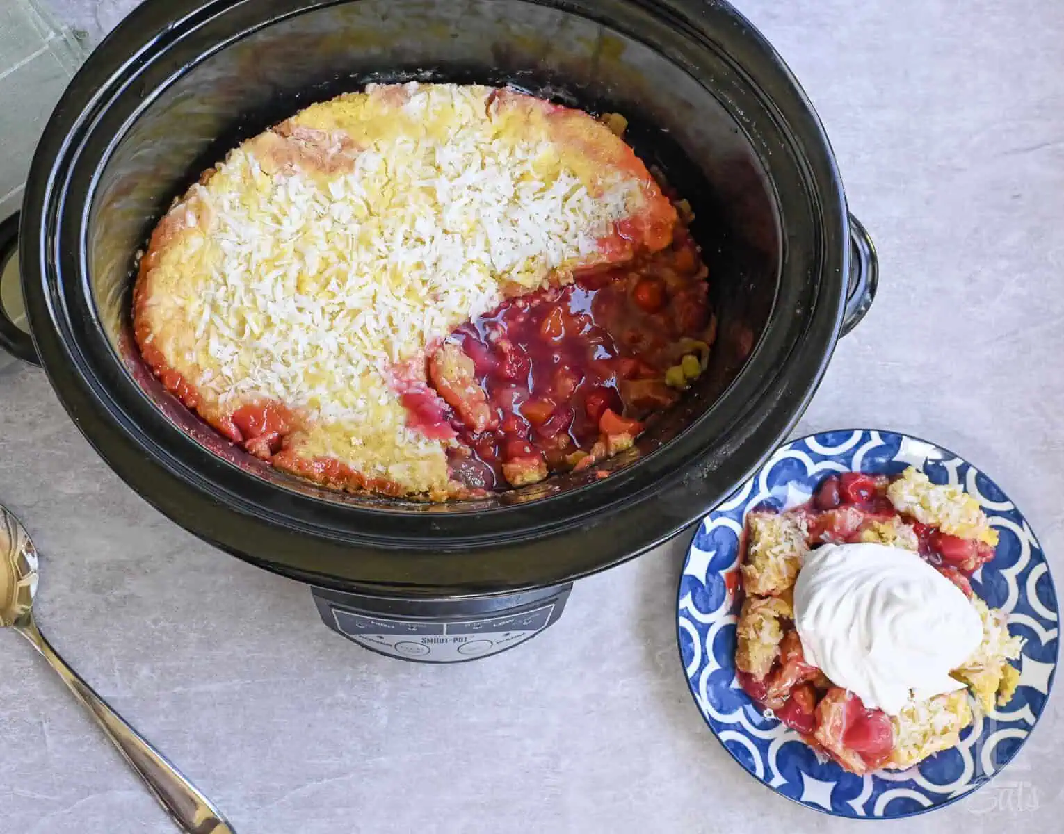 tropical dump cake in a crock pot, next to serving plate.