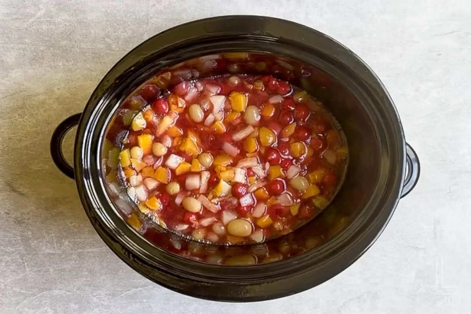 cherry pie filling and fruit cocktail mixed together in a slow cooker.