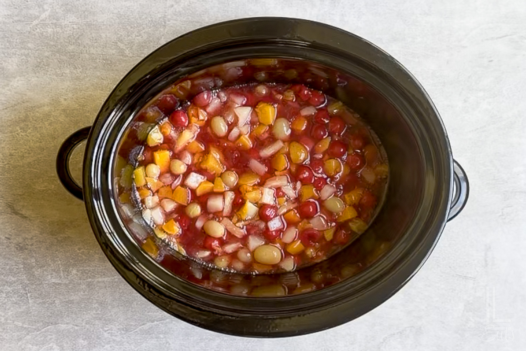 cherry pie filling and fruit cocktail mixed together in a slow cooker.