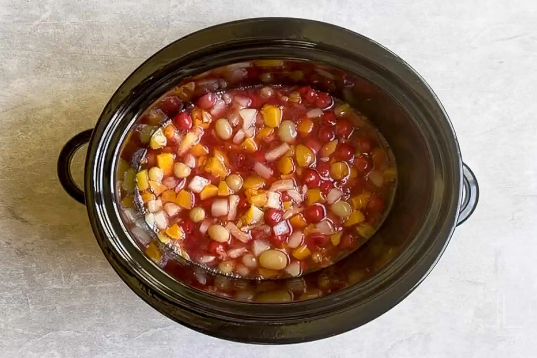 cherry pie filling and fruit cocktail mixed together in a slow cooker.