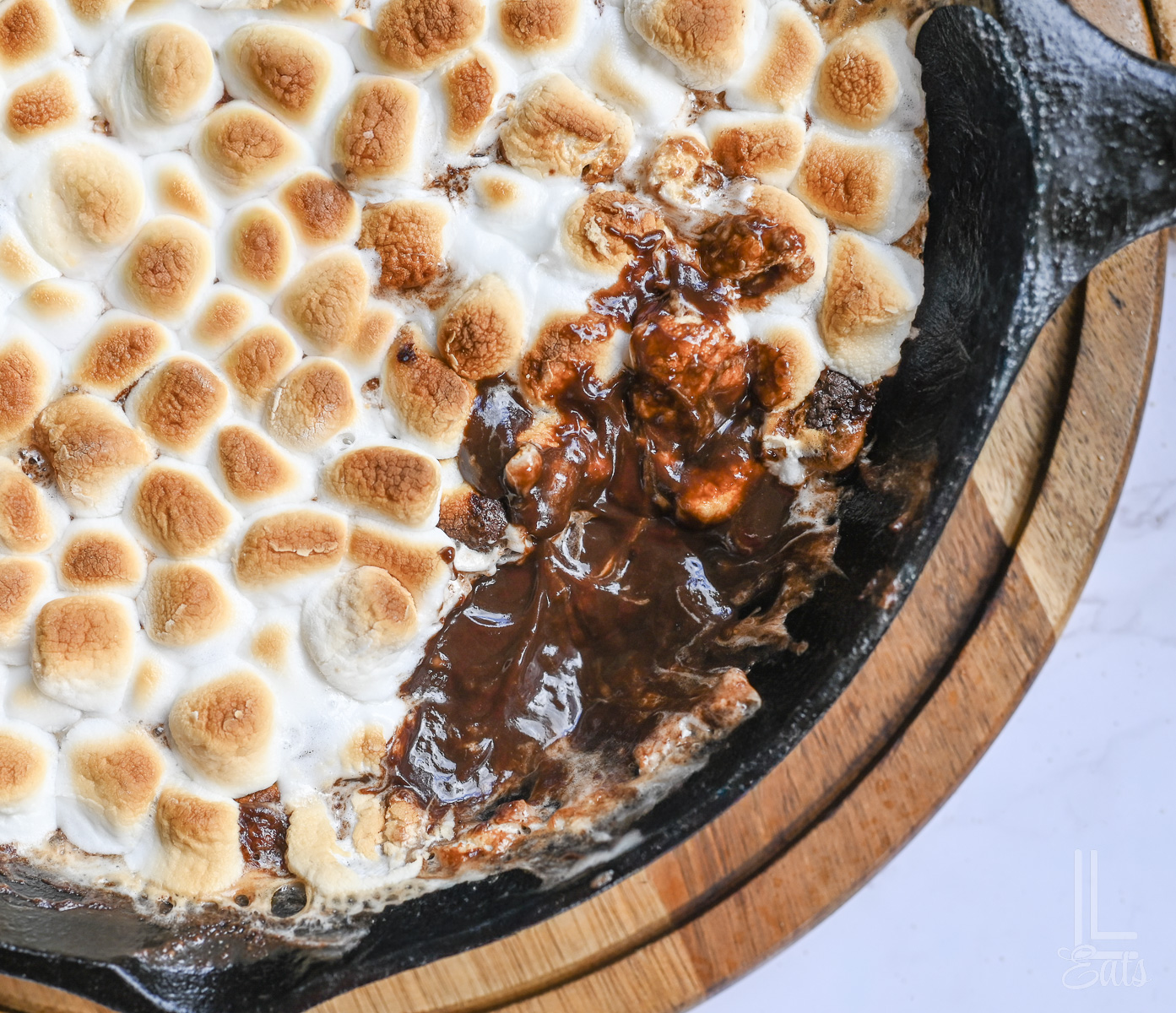 smores dip with marshmallows missing from a corner, revealing a melted chocolate layer.