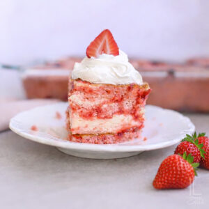 piece of strawberry earthquake cake topped with whipped cream and a strawberry.