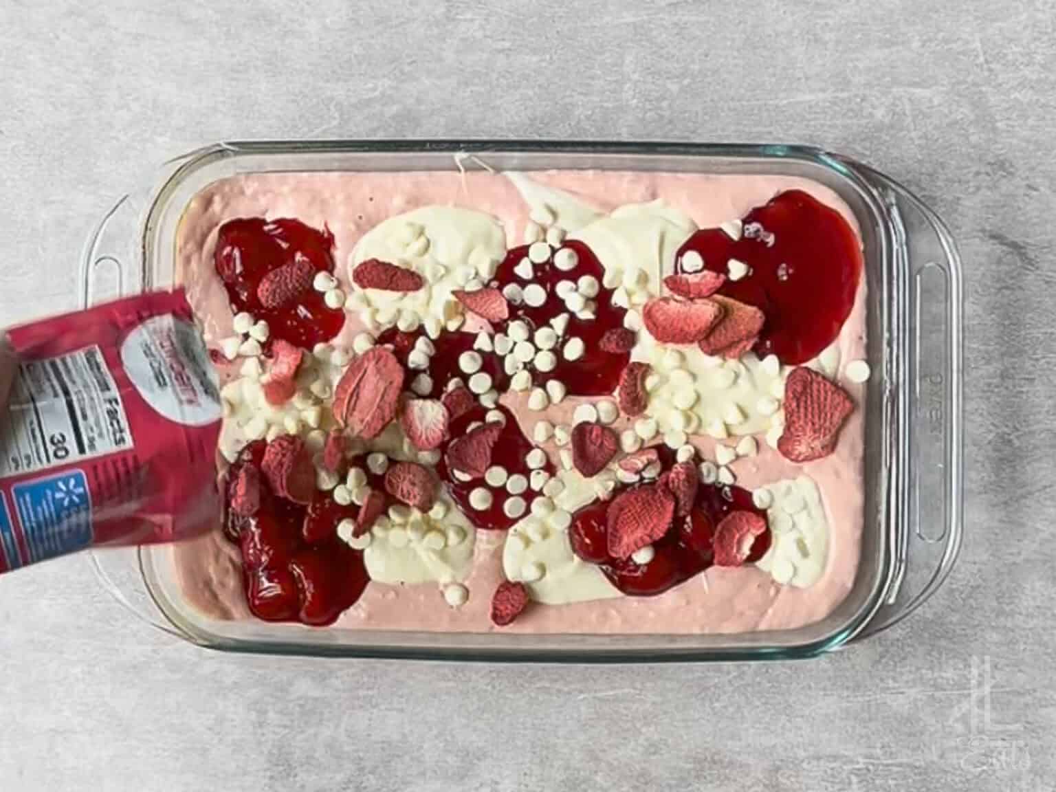 pouring freeze-dried strawberries over the cake batter, topped with pie filling and white chocolate chips.
