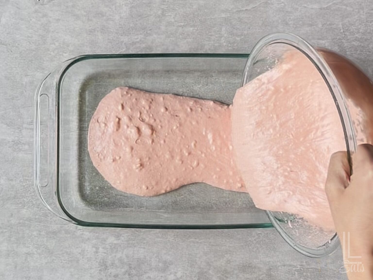 pouring strawberry cake batter into a 9x13" dish.