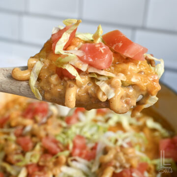 holding taco mac and cheese, topped with lettuce and tomato, in a spoon.
