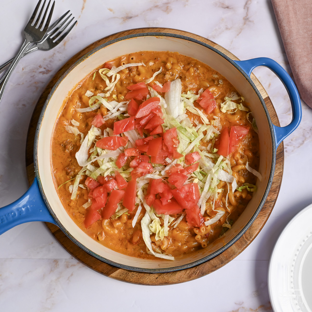 large skillet of taco mac and cheese, topped with chopped tomatoes and shredded lettuce.