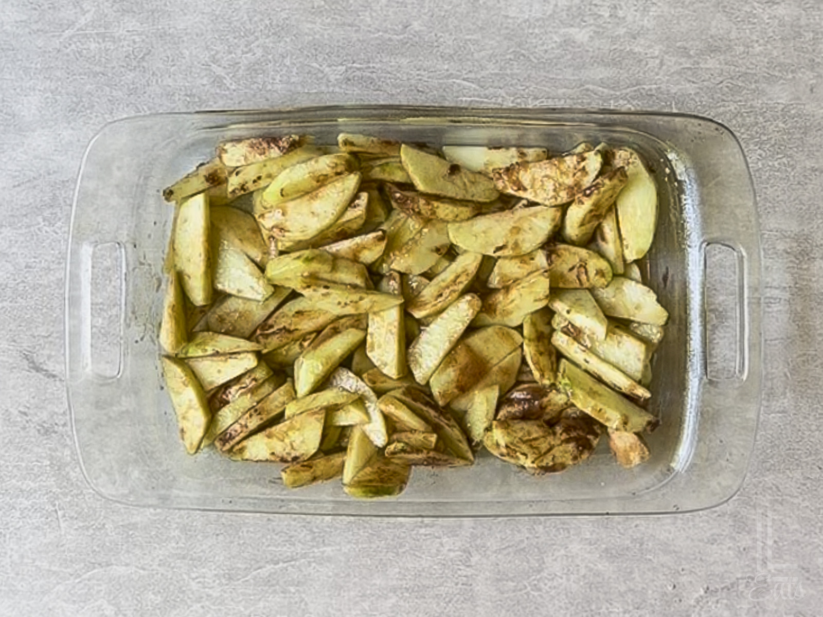sliced apples covered with brown sugar, cinnamon, and butter in a glass baking dish.