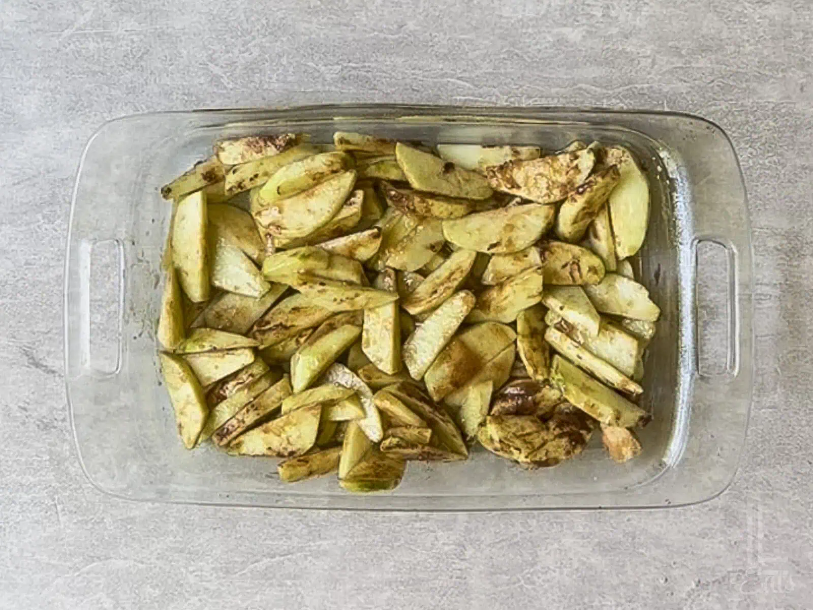 sliced apples covered with brown sugar, cinnamon, and butter in a glass baking dish.
