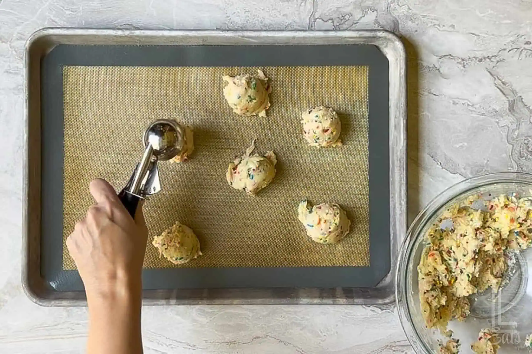 scooping funfetti cookies onto a lined cookie sheet with a cookie scoop.