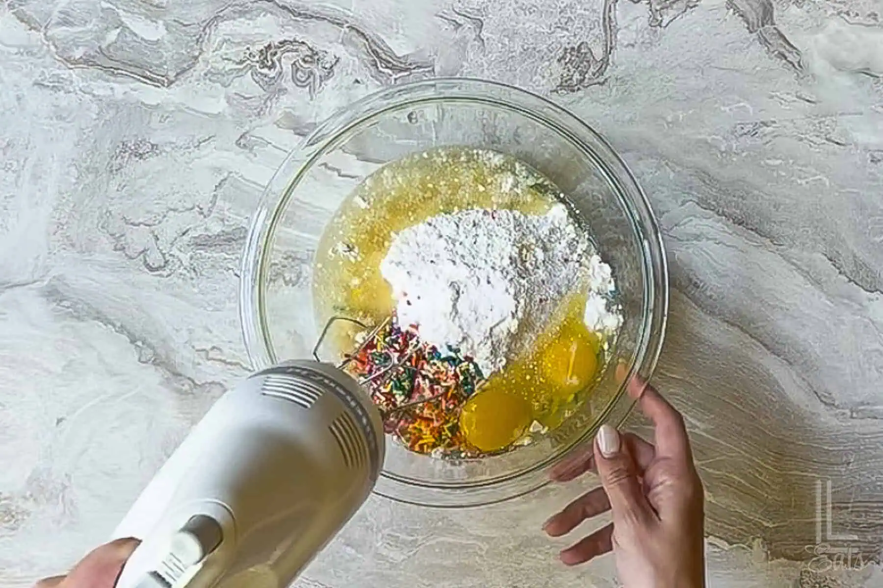 mixing ingredients for funfetti cookies in a bowl with a hand mixer.