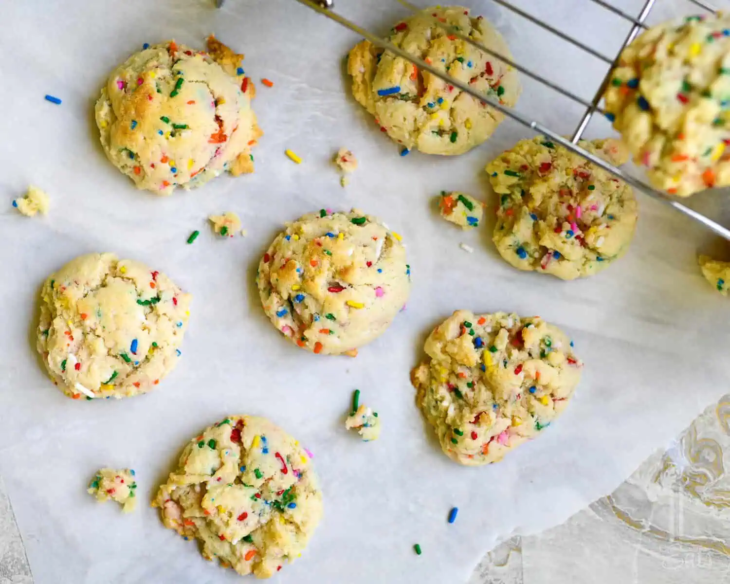 funfetti cake mix cookies on a piece of parchment paper, next to a baking rack.