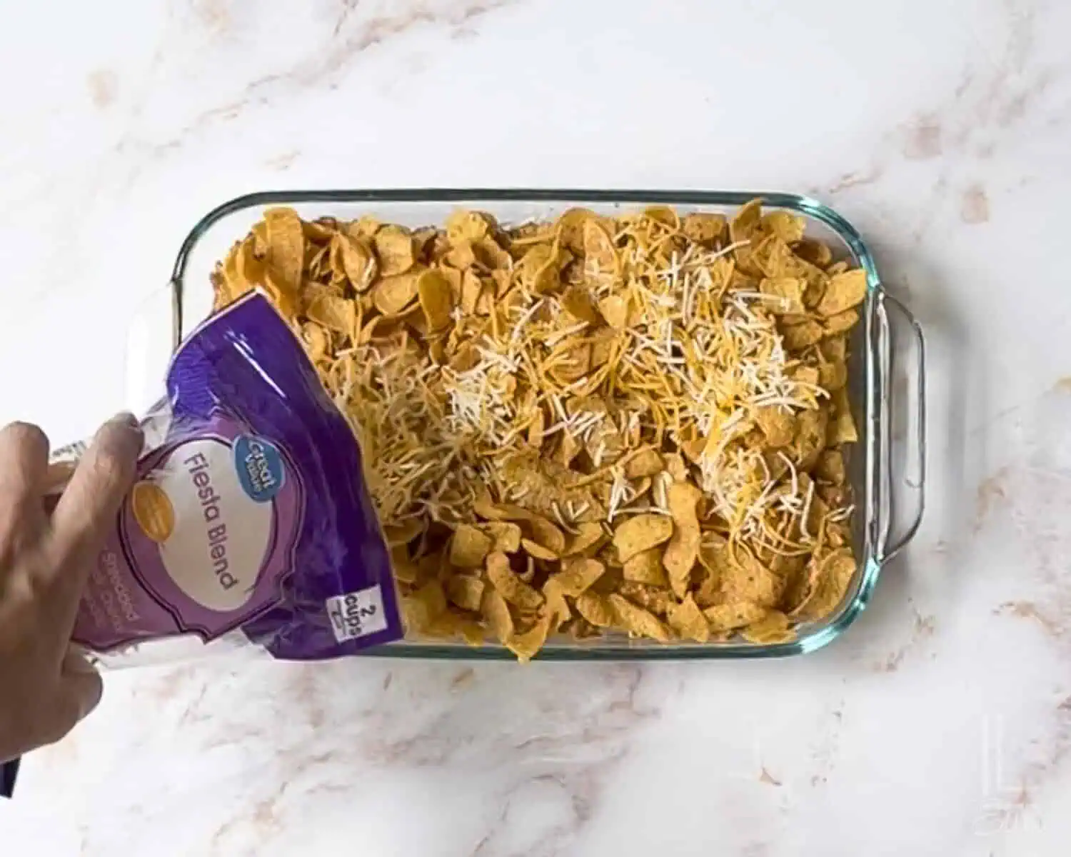 adding shredded cheese to the top of the walking taco casserole before baking.