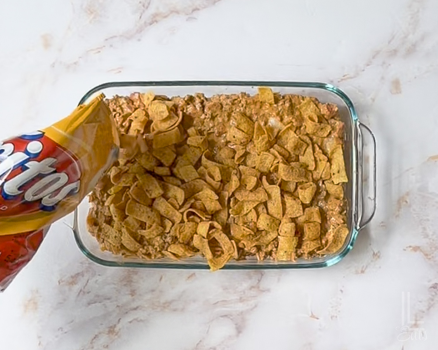 sprinkling fritos over the top of the walking taco casserole meat mixture.