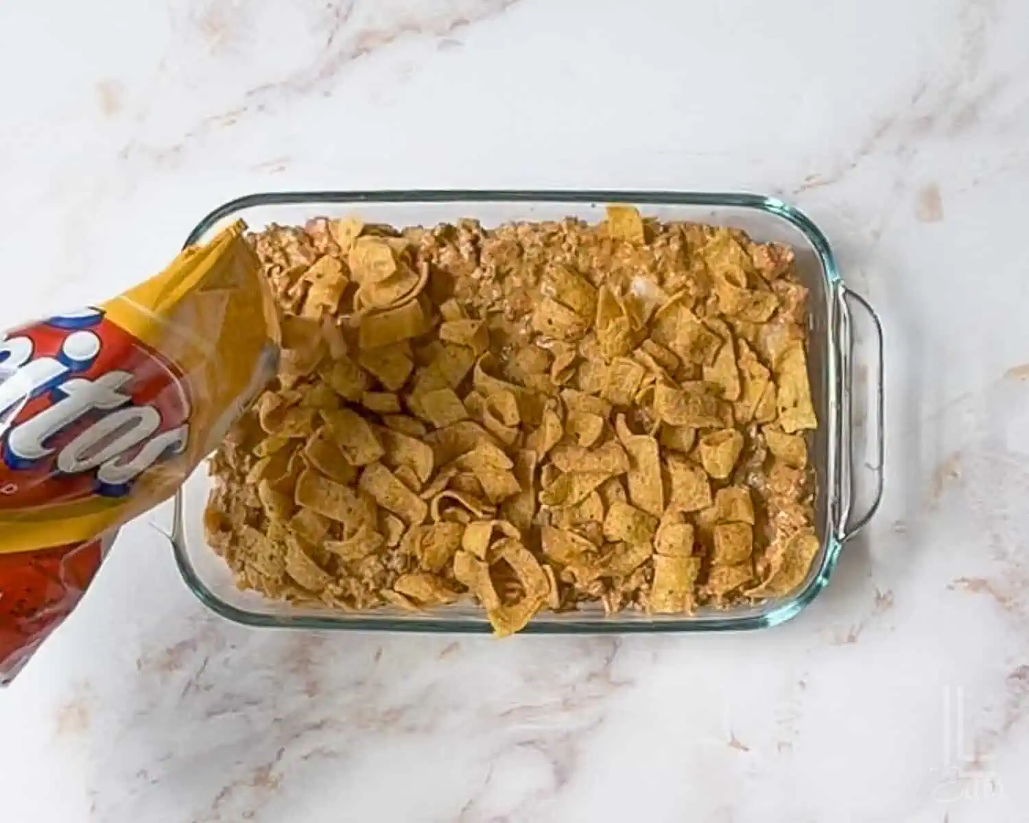 sprinkling fritos over the top of the walking taco casserole meat mixture.