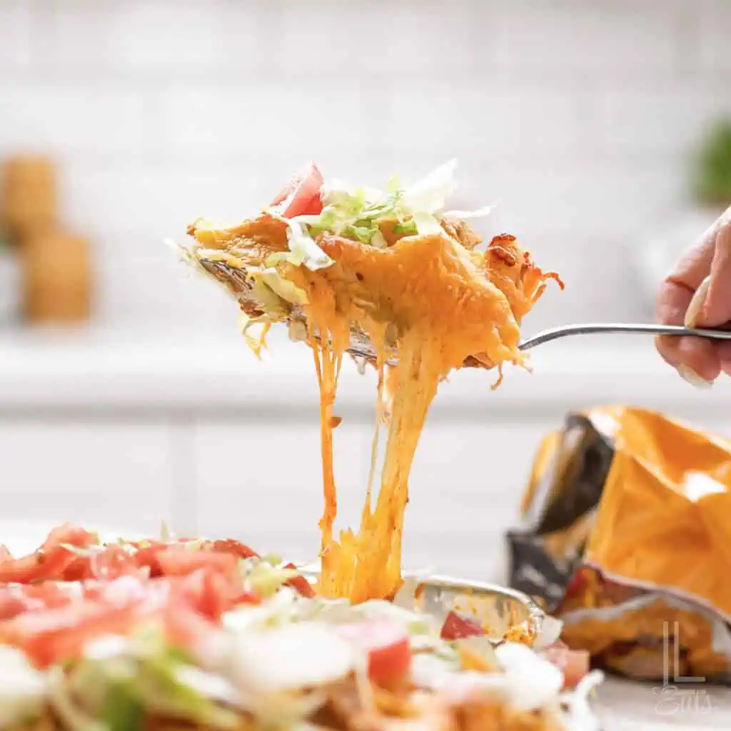 holding a spoonful of cheesy walking taco casserole topped with lettuce and tomato.