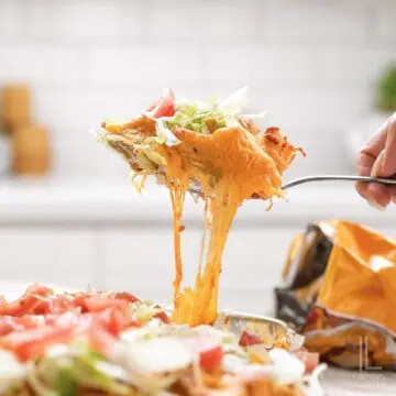holding a spoonful of cheesy walking taco casserole topped with lettuce and tomato.