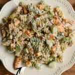 Bacon cheddar pickle pasta salad on a white plate with ingredients around it.