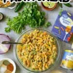 Elote Pasta Salad with fresh herbs, lime, and corn in a glass bowl on a kitchen counter.