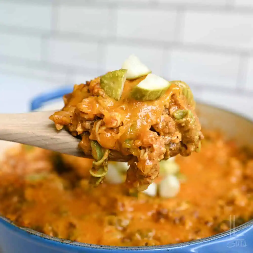 holding a spoonful of cheeseburger pasta over a pot full of food.