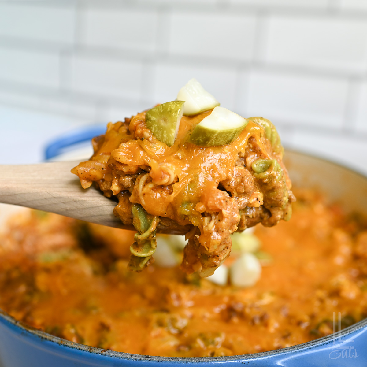 holding a spoonful of cheeseburger pasta over a pot full of food.