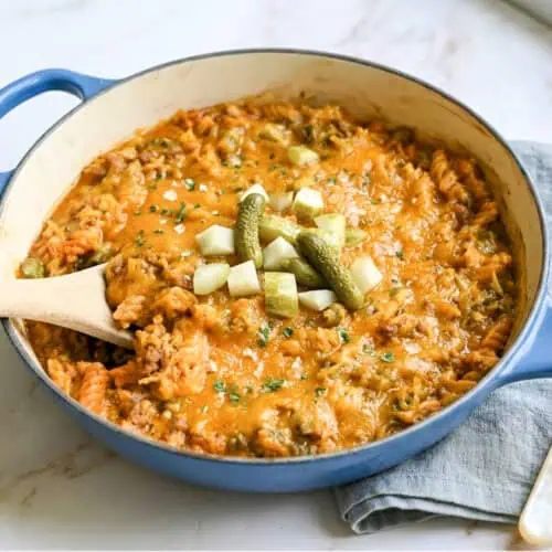 a large pot of cheeseburger pasta, topped with melted cheddar cheese, with a wooden spoon.