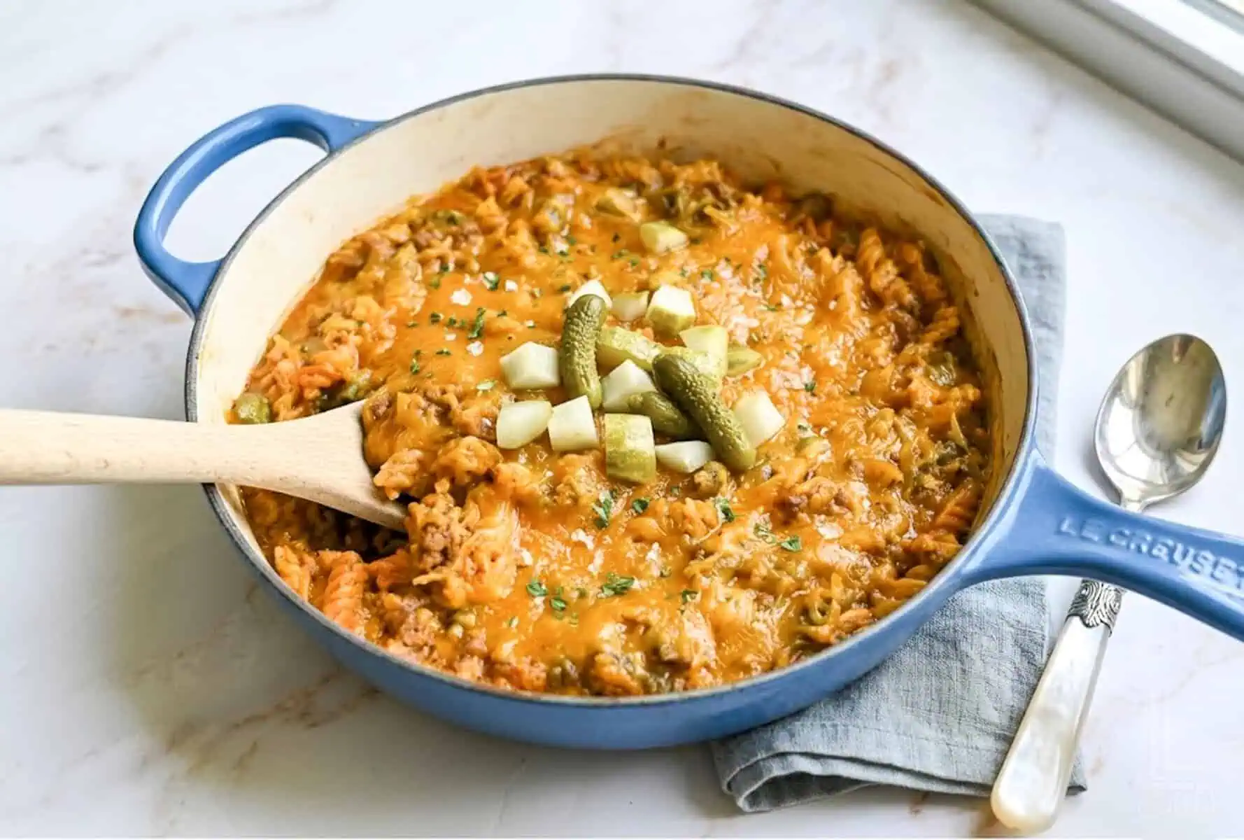 a large pot of cheeseburger pasta, topped with melted cheddar cheese, with a wooden spoon.