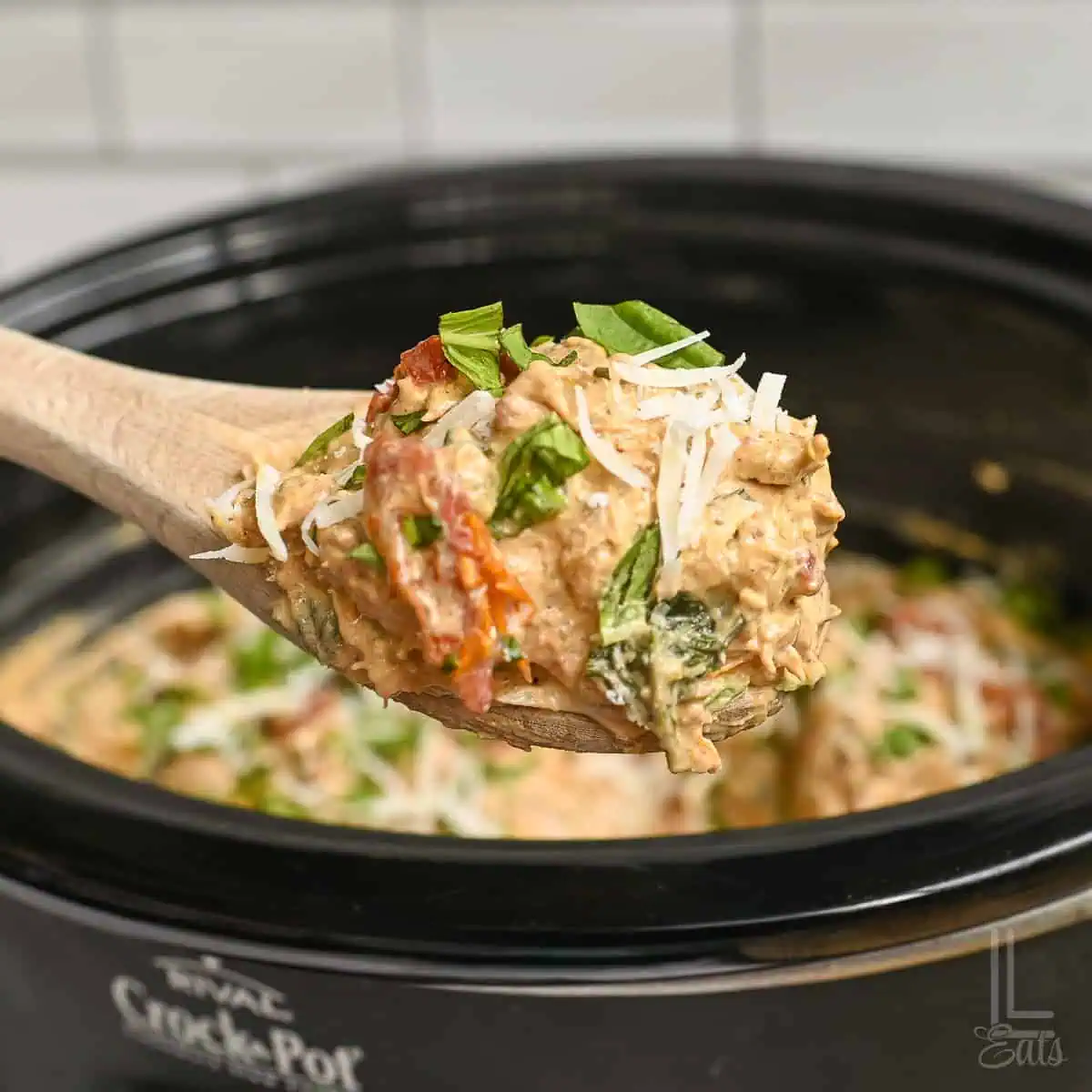 holding a spoonful of marry me chicken in front of a crock pot.