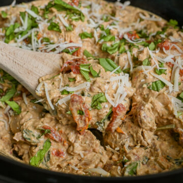close up of marry me chicken in a crock pot, covered in basil and parmesan, with a spoon.